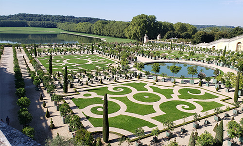 En el corazón del jardín, rodeado de exuberantes áreas verdes, se alza la majestuosa fuente como pieza central del jardín barroco de Versalles.