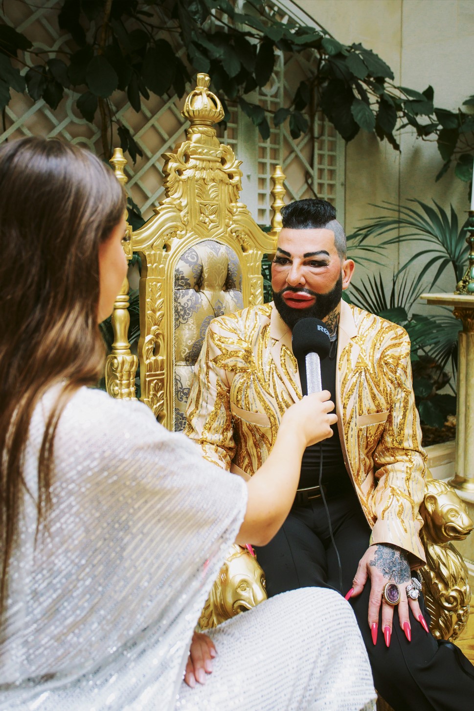 Harald Glööckler assis sur un trône doré avec une couronne, dans une interview avec Leni Summer.