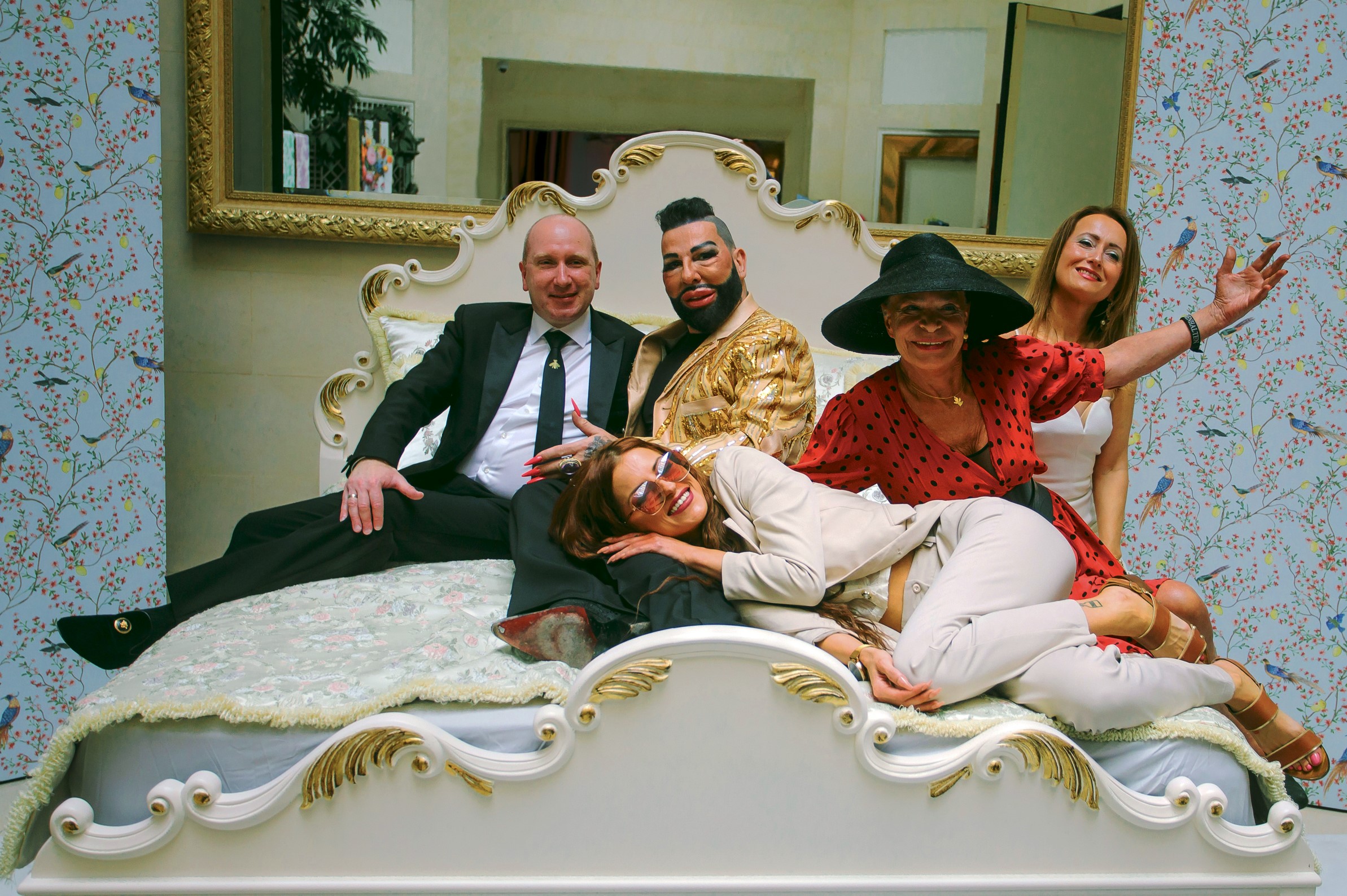 You see Harald Glööckler in a bed with Princess Xenia of Saxony, Barbara Engel, Dr Sina Schertl and Marvin Schert at the presentation of the Pompöös Provence collection at the Hotel Adlon in Berlin.