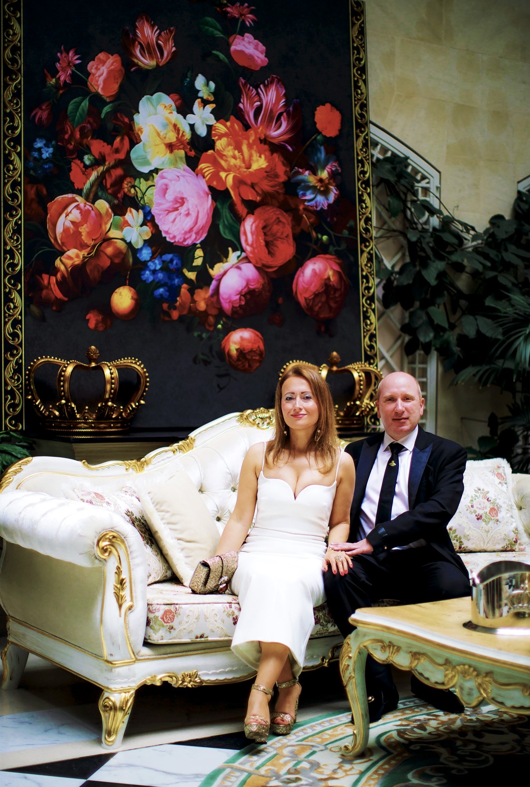 Sie sehen Frau Dr Sina Schertl und Herr Marvin Schertl auf einem Barock Landhausstil Sofa in Weiß Gold der neuen Kollektion Pompöös Provence by Casa Padrino