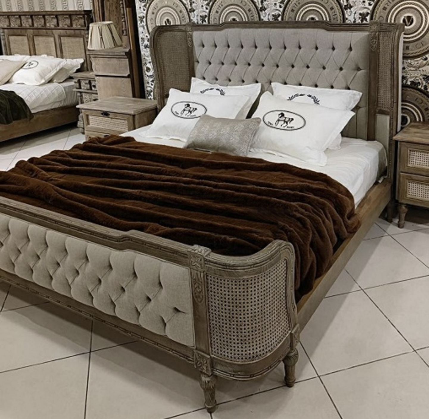 You see a luxurious solid double bed on feet with upholstered head and footrests and rattan weave from the Harald Glööckler Pompöös Provence collection 2024 in a baroque country house style in the colors brown gray made of solid wood.