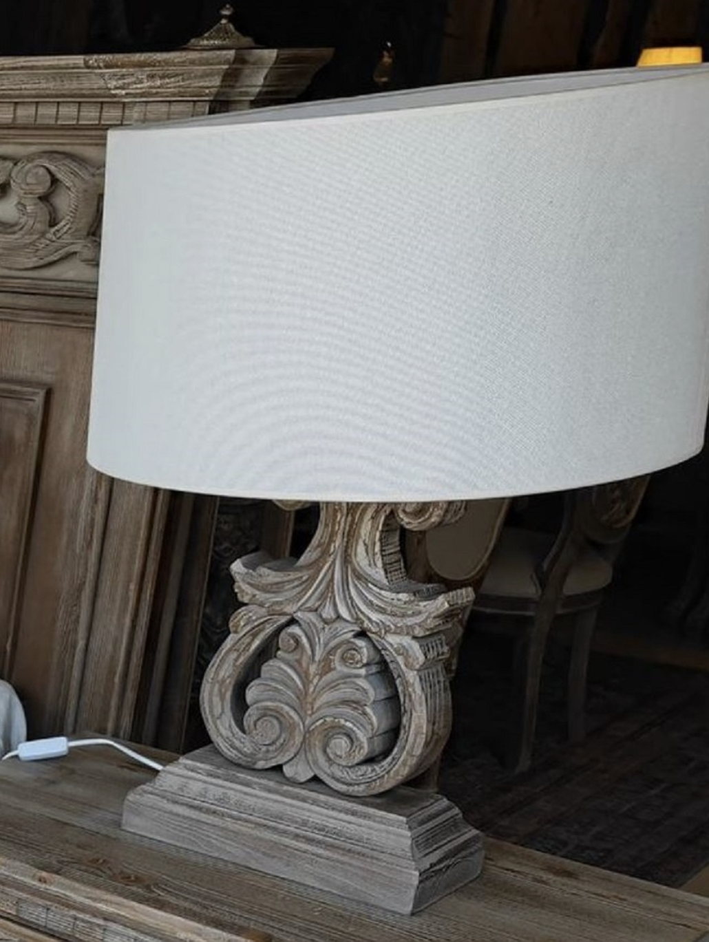 Vous voyez une luxueuse lampe de chevet sculptée à la main de la collection Harald Glööckler Pompöös Provence 2024 dans un style maison de campagne baroque dans les couleurs marron gris en bois massif et tissu le plus fin.