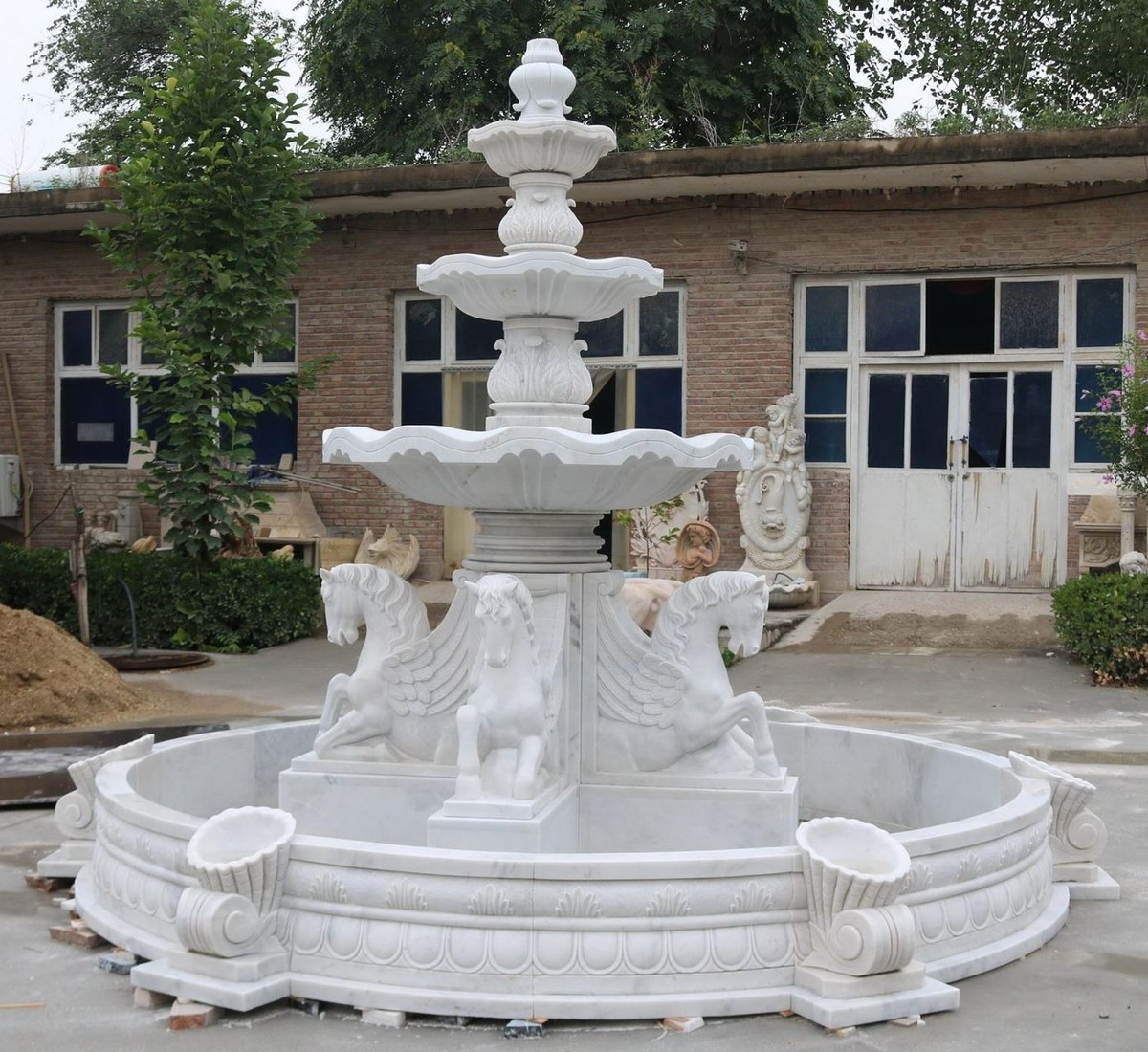 Vedrai una maestosa fontana a tre livelli con un bordo rotondo decorato. Ai piedi della fontana ci sono quattro figure di Pegaso. Il colore è bianco.