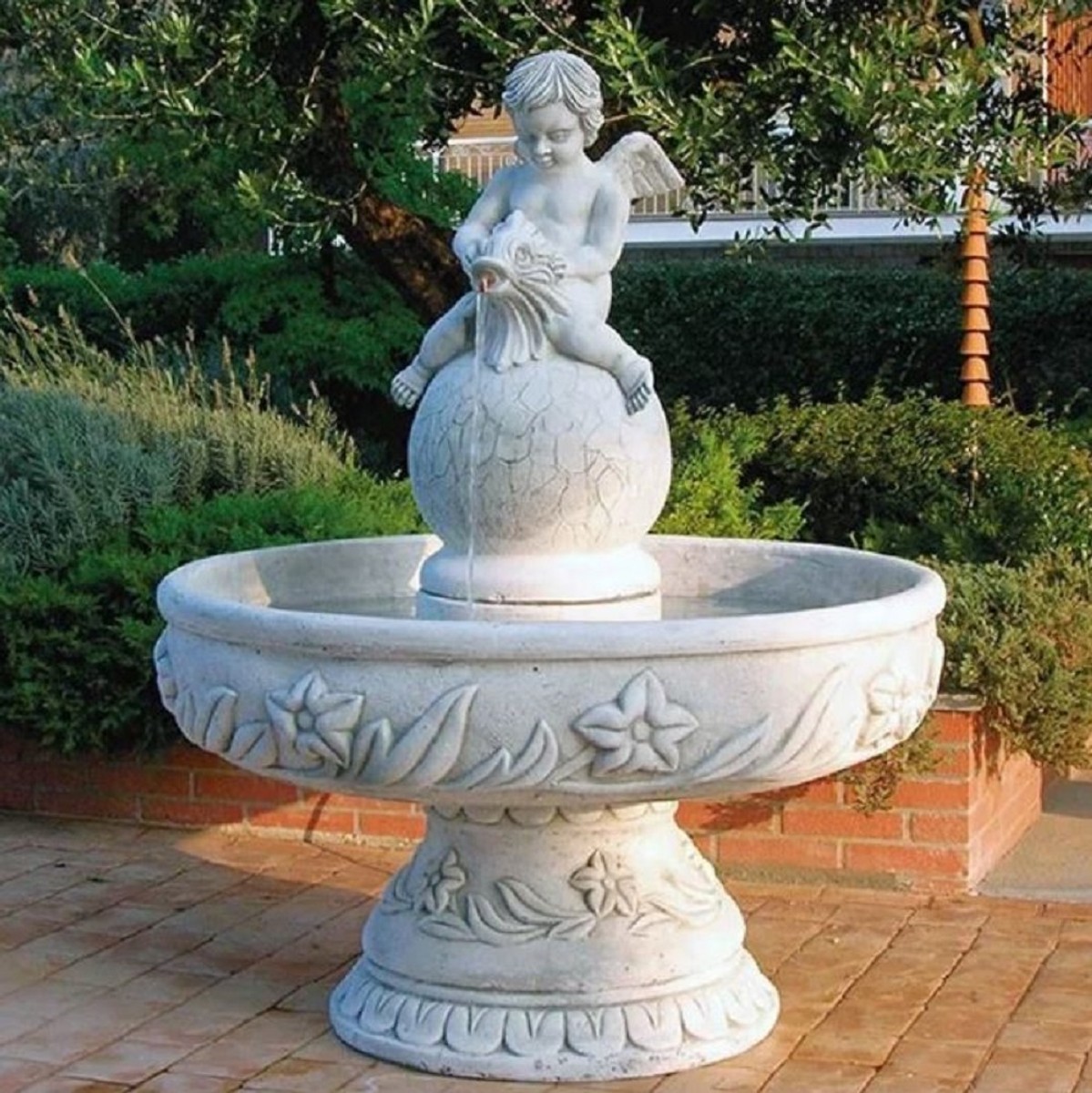 You see a beautiful water feature in the form of a round fountain, in the middle there is a ball on which an angel sits. Color: white, gray.